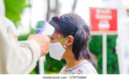 Temperature Check In School Kid Girl At School.Open School First Health Check Up Measurement.Asian Girl Measuring Body Temperature And Wearing A Face Mask Before Go Back To School.Healthcare Medical.