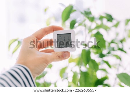Temperature and humidity meter in a female hand on plants background. Comfortable climate at home.