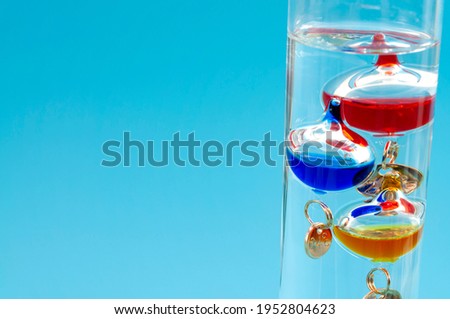 Temperature measurement instruments, educational tools, meteorology concept with Galileo thermometer made of coloured glass balls in a water filled cylinder isolated on blue background with copy space