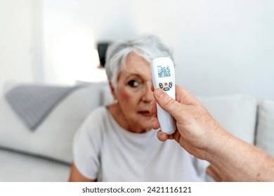 Temperature screening. Doctor visit a senior woman at home. Doctor or healthcare worker with senior adult female patient in hospital or clinic checking fever with infrared thermometer. - Powered by Shutterstock