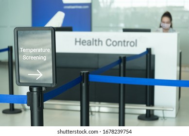 Temperature Screening Sign At Airport With Woman Wearing Mask Sitting At Health Control Counter