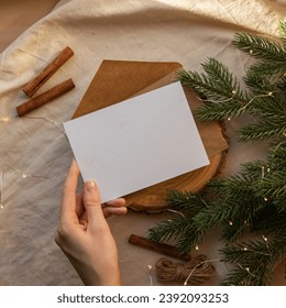 Template for Christmas greeting card. Hand holds empty sheet of paper with Christmas tree branch and cinnamon sticks on background. Square horizontal mock up for New Year postcard - Powered by Shutterstock