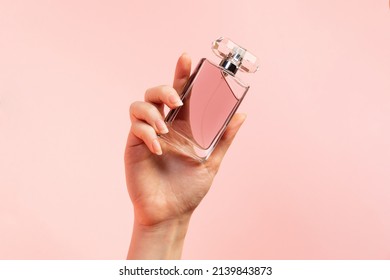 A template for perfume and toilet water. A woman's hand elegantly holds a glass perfume bottle on a pink background, close-up. Copy space. The concept of perfumery and beauty.