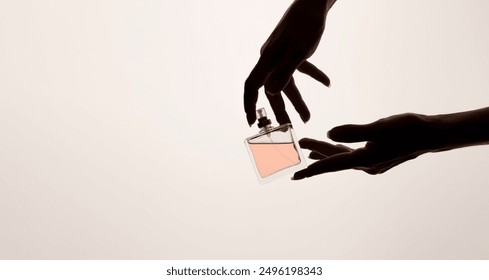 A template for perfume and toilet water. A woman's hand elegantly holds a glass perfume bottle on a pink background, close-up. Copy space.