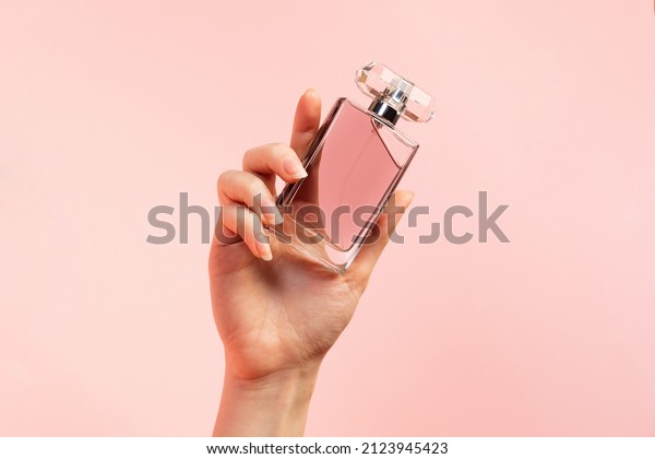A template\
for perfume and toilet water. A woman\'s hand elegantly holds a\
glass perfume bottle on a pink background, close-up. Copy space.\
The concept of perfumery and\
beauty.