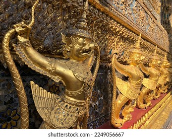 Temple of the Emerald Buddha.The central base of the ordination hall is decorated with a golden row of Garudas. each grasping within its claws two Naga serpents, surround all of the ordination hall. - Shutterstock ID 2249056667