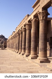 Temple of Philae orderly decorated stone columns fronted by stone courtyard with clear blue sky above, Aswan, Egypt.