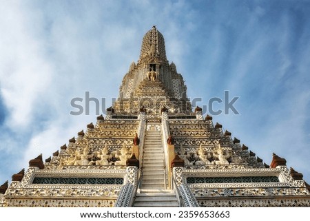 A temple in Thailand with a tall, ornate spire and a staircase leading up to it. The spire is decorated with intricate patterns and designs. wat arun