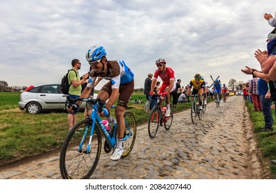 Templeuve, France - April 08, 2018: The peloton riding on the cobblestone road in Templeuve in front of the traditional Vertain Windmill during Paris-Roubaix 2018. 