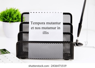 Tempora mutantur et nos mutamur in illis Translated from Latin, it means Times are changing, and we are changing with them. on a white sheet of a notebook in a black stand. Concept photo