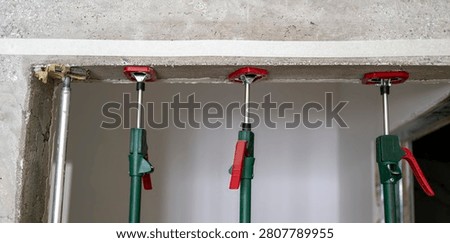 Temporary construction shoring system with adjustable steel props supporting a load-bearing wall while reinforcement and concrete harden on an active building site