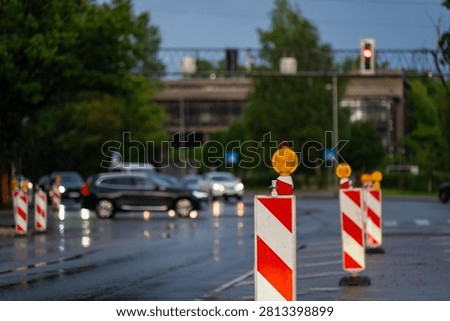 Temporary road work delineator with amber warning beacon on a rain soaked urban street, highlighting traffic management, lane closure safety, highway maintenance, and transport engineering