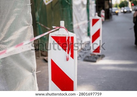 Temporary traffic control barriers and red barrier tape signaling a hazardous road repair area and blocking public pedestrian thoroughfare passage