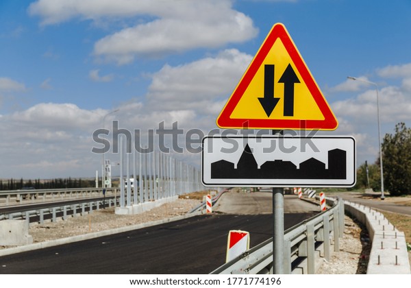 Temporary traffic sign two-way traffic and\
traffic sign the beginning of the village against the sky and the\
road under\
construction.