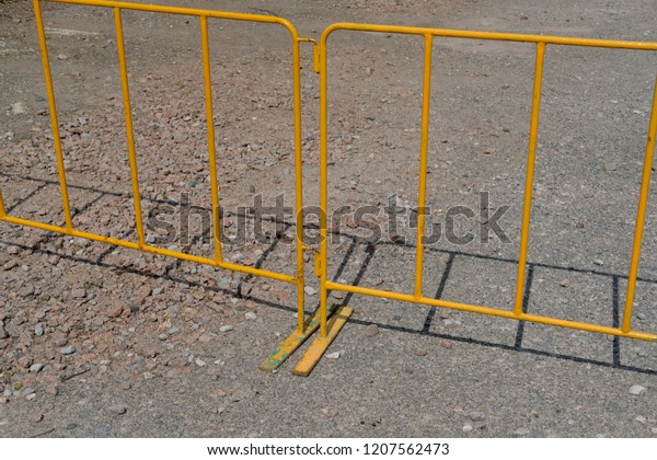 temporary yellow fence or barrier on a gravel\
car park in bright\
sunlight