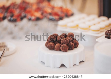 A tempting array of chocolate truffles sits on a delicate white stand. This scrumptious treat is part of a lavish dessert spread at a vibrant celebration, inviting guests to indulge.
