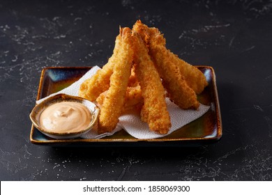 Tempura deep-fried EBI prawns with spiced sauce on a plate on a dark background. Appetizer in the style of Japanese cuisine. Deep-fried shrimp in breeding close-up. Horizontal photo.
