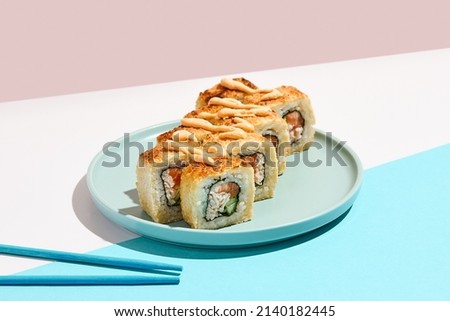Tempura maki roll on ceramic plate with chopsticks. Hot sushi with salmon, crab and cucumber inside, spicy mayo topped. Modern japanese menu concept. Maki sushi on coloured background