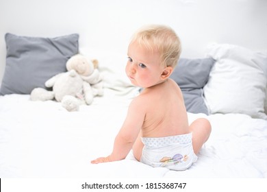 Ten Month Baby Boy Sitting On Bed And Looking Back. Little Kid In Nappy At Home. Little Naked Kid In Nappy. Back View. Byby Care Concept, Banner Copy Space