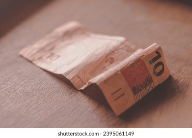 Ten Reais bill, 10 reais on a wooden table with natural light, Brazilian money, ten reais bill. - Shutterstock ID 2395061149