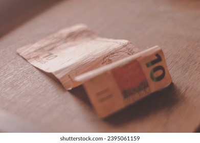 Ten Reais bill, 10 reais on a wooden table with natural light, Brazilian money, ten reais bill. - Shutterstock ID 2395061159