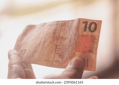 Ten Reais bill, 10 reais on a wooden table with natural light, Brazilian money, ten reais bill. - Shutterstock ID 2395061165