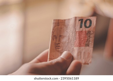 Ten Reais bill, 10 reais on a wooden table with natural light, Brazilian money, ten reais bill. - Shutterstock ID 2395061189