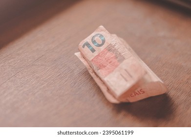 Ten Reais bill, 10 reais on a wooden table with natural light, Brazilian money, ten reais bill. - Shutterstock ID 2395061199