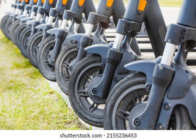 Ten scooters lined up in a summer parking lot. The image shows only the front wheels of the vehicles. - Shutterstock ID 2155236453