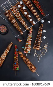 ten waffles sticks of diferents flavors, cereal, chocolate icing, vanilla icing, marshmallows, chocolate candies, chocolate cookies, bananas, strawberries, black background

