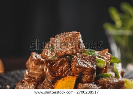 Tender beef cubes expertly seared and glazed, garnished with fresh herbs and vegetables on elegant plate against dark background for gourmet dining presentation.