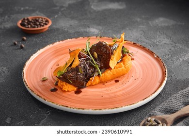 Tender braised beef cheeks served atop smooth pumpkin puree, garnished with microgreens, on a ceramic plate over a black concrete background. - Powered by Shutterstock