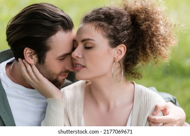 Tender And Curly Woman Touching Face Of Bearded Man In Park