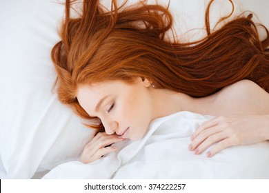 Tender cute young woman with long red hair lying and sleeping in bed