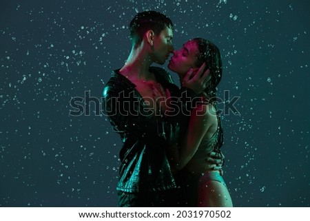 Tender feelings. Young couple, man and woman hugging, kissing under the rain over dark background in neon light. Concept of human emotions and feelings, love, passion, tenderness