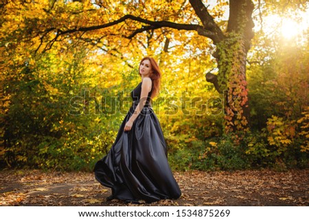 tender girl in a black dress strolls against the background of fiery autumn nature.