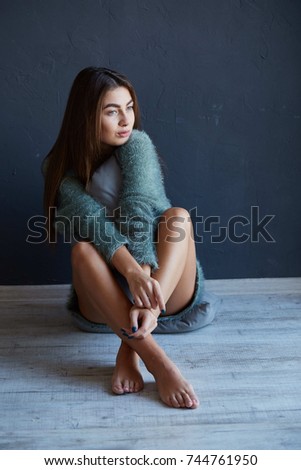 Tender girl newly awake posing sitting on a pillow in a blue sweater