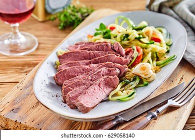 Tender gourmet beef fillet arranged in slices served with a raw fresh vegetable salad with seasoning and a glass of red wine for a low carbohydrate meal