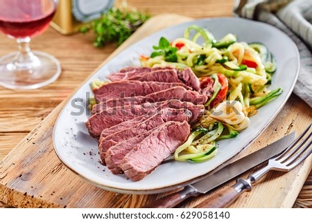 Tender gourmet beef fillet arranged in slices served with a raw fresh vegetable salad with seasoning and a glass of red wine for a low carbohydrate meal