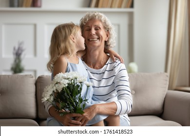 Tender little granddaughter kiss on cheek old grandmother today she is birthday girl. Small kid congratulates granny with Women Day 8-march express love make surprise gave flowers as pleasant gesture