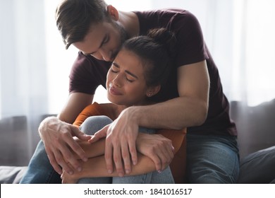 Tender Man Calming Frustrated Girlfriend Crying On Sofa At Home