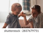 A tender moment between two young sisters as they connect and hold hands in a softly lit indoor environment