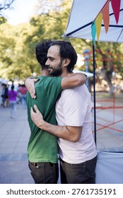 A tender moment captured between two men sharing a hug amidst a lively outdoor event, showcasing connection and joy