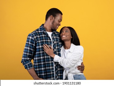 Tender moment, young romantic couple enjoying, married people have fun at date. Happy african american guy and lady hugs and looks at each other, isolated on yellow background, studio shot, free space