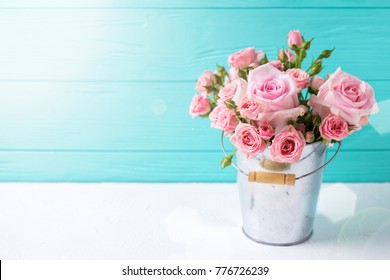 Tender pink roses flowers in pot on white wooden background against turquoise wall. Floral still life.  Selective focus. Place ffor text. 