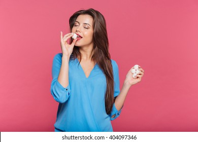 Tender Pretty Young Woman With Eyes Closed Eating Sweet Candies Over Pink Background