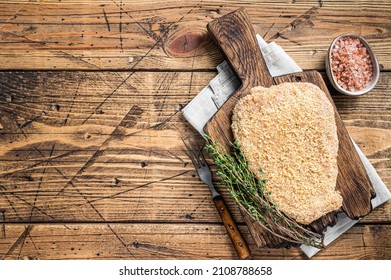 Tender Raw Breaded Wiener schnitzel on a wooden board with thyme. wooden background. Top view. Copy space