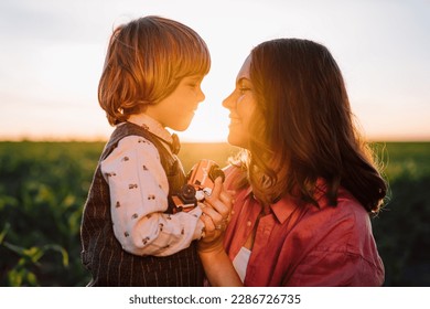 Tender scene of loving son with mom on sunset backdrop. Beautiful family. Cute 3 year old kid with mother. Parenthood, childhood, happiness, children wellbeing concept. High quality photo