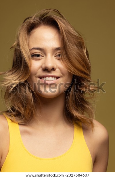 Tender smile. Close-up portrait of\
young happy caucasian woman isolated on dark yellow background.\
Concept of female beauty, tenderness, positive\
lifestyle.