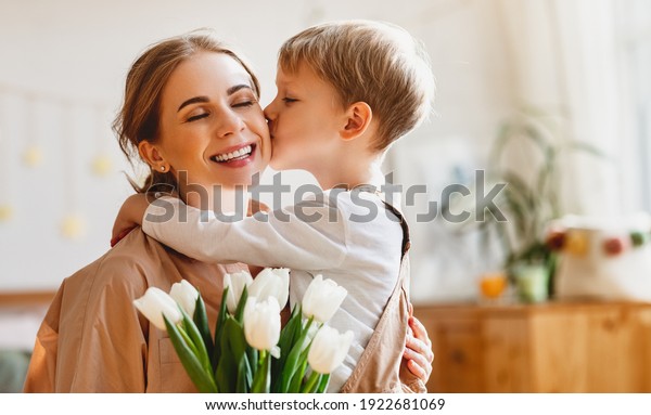 tender son kisses the happy mother and gives her a\
bouquet of tulips, congratulating her on mother\'s day during\
holiday celebration at\
home